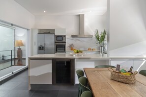 Una cocina moderna con horno empotrado, microondas y un refrigerador pequeño. Hay un comedor con una mesa y sillas de madera.