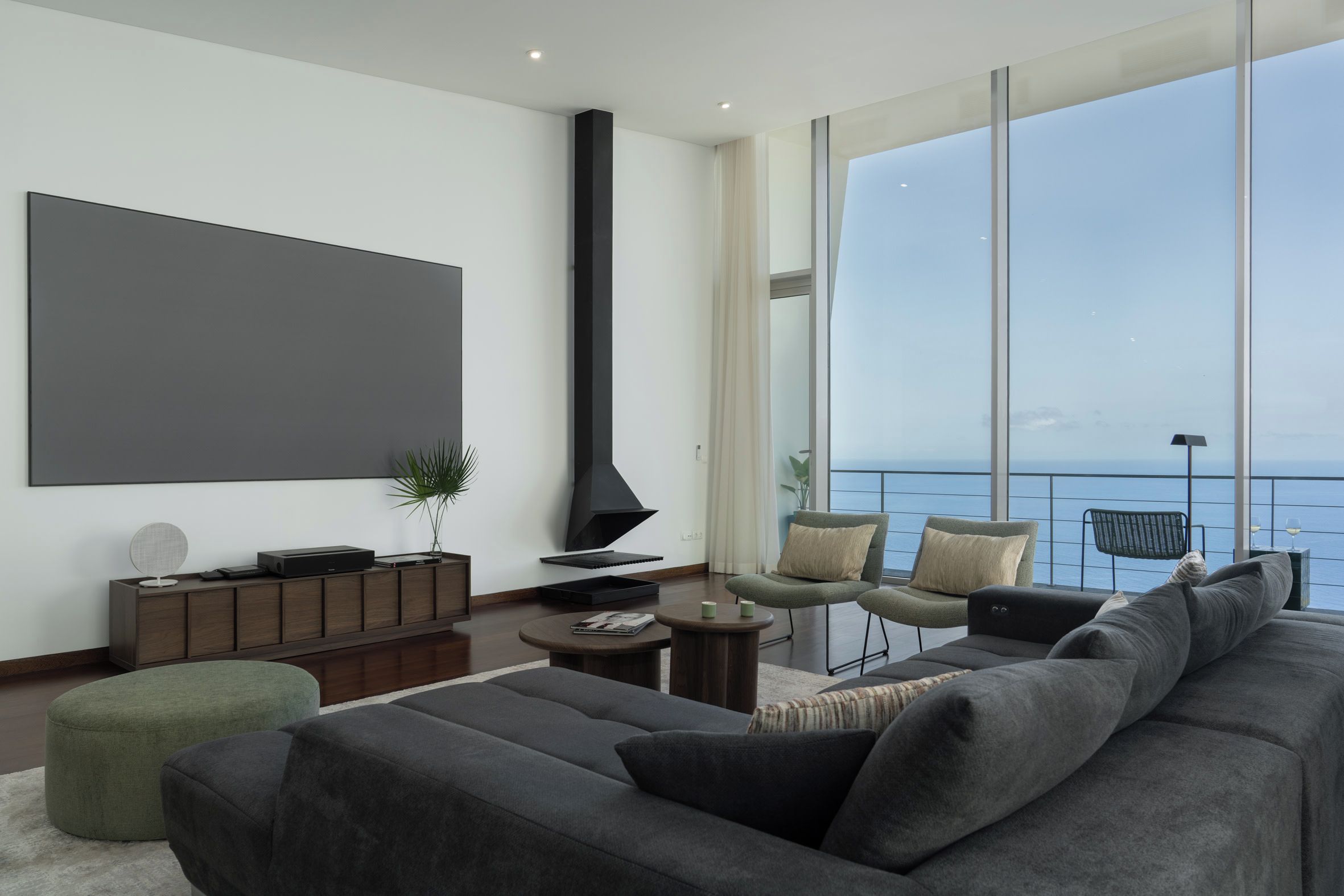 A modern living room with a large flat-screen TV, a fireplace, and a view of the sea.