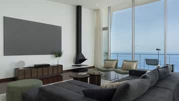 A modern living room with a large flat-screen TV, a fireplace, and a view of the sea.