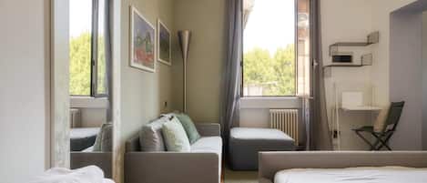 A hotel room with a bed, a sofa, a chair, a radiator, and a window with curtains.