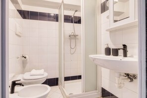 Een badkamer met toilet, bidet en douche met glazen deur.