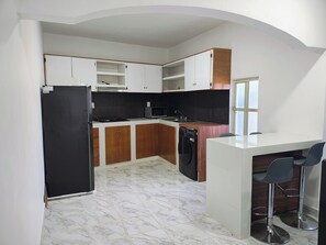 A kitchen with a stove, microwave, and dishwasher, a white countertop, and a bar area with two stools.