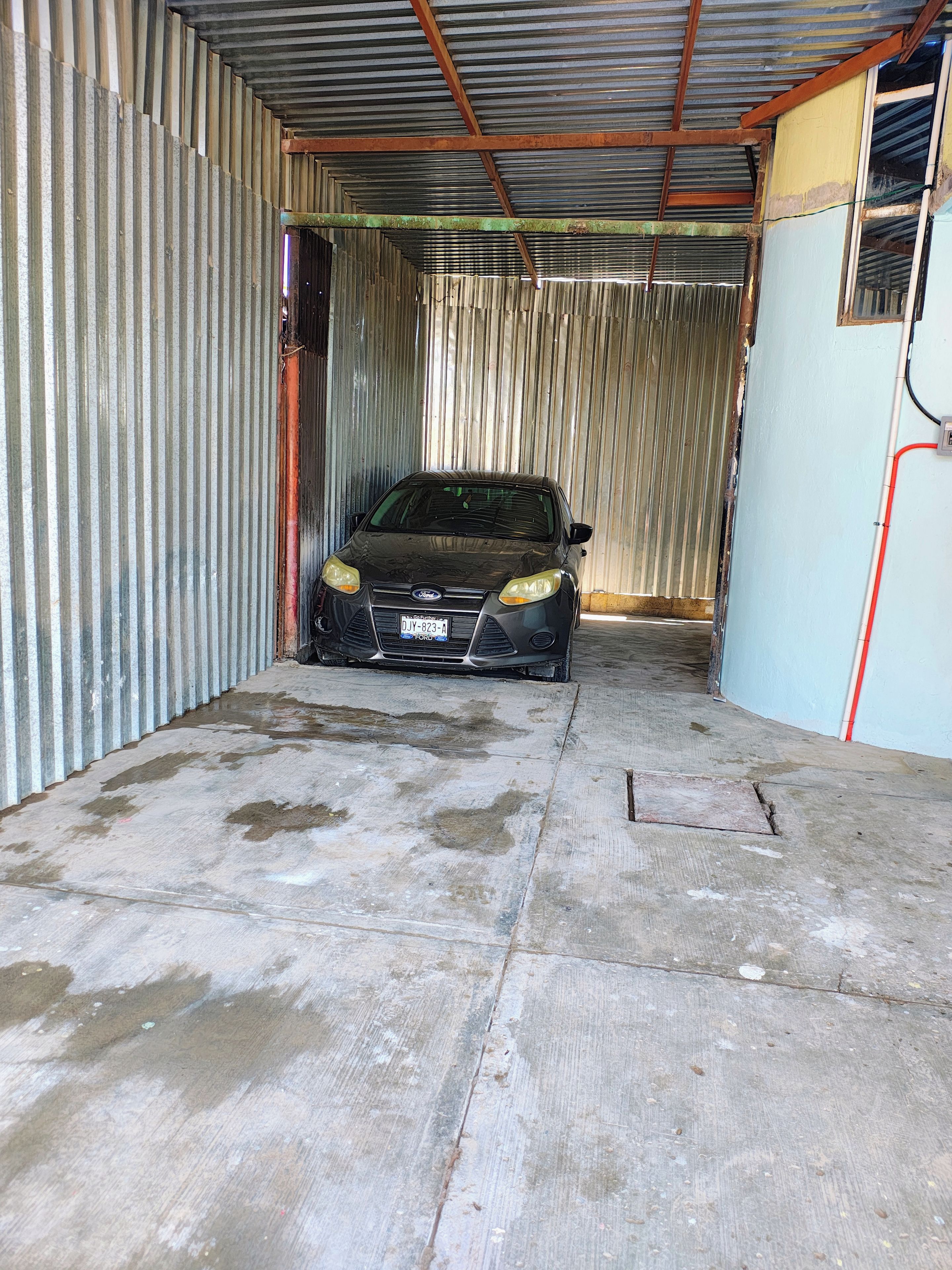 Ein Auto in einer Garage mit wellenförmigen Metallwänden und einem Betonboden.