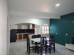 A dining area with a table and chairs, a kitchen in the background, and a teal accent wall.