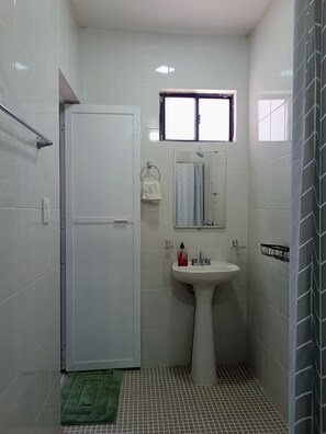 A small bathroom with a white door, a window, a sink, and a mirror.