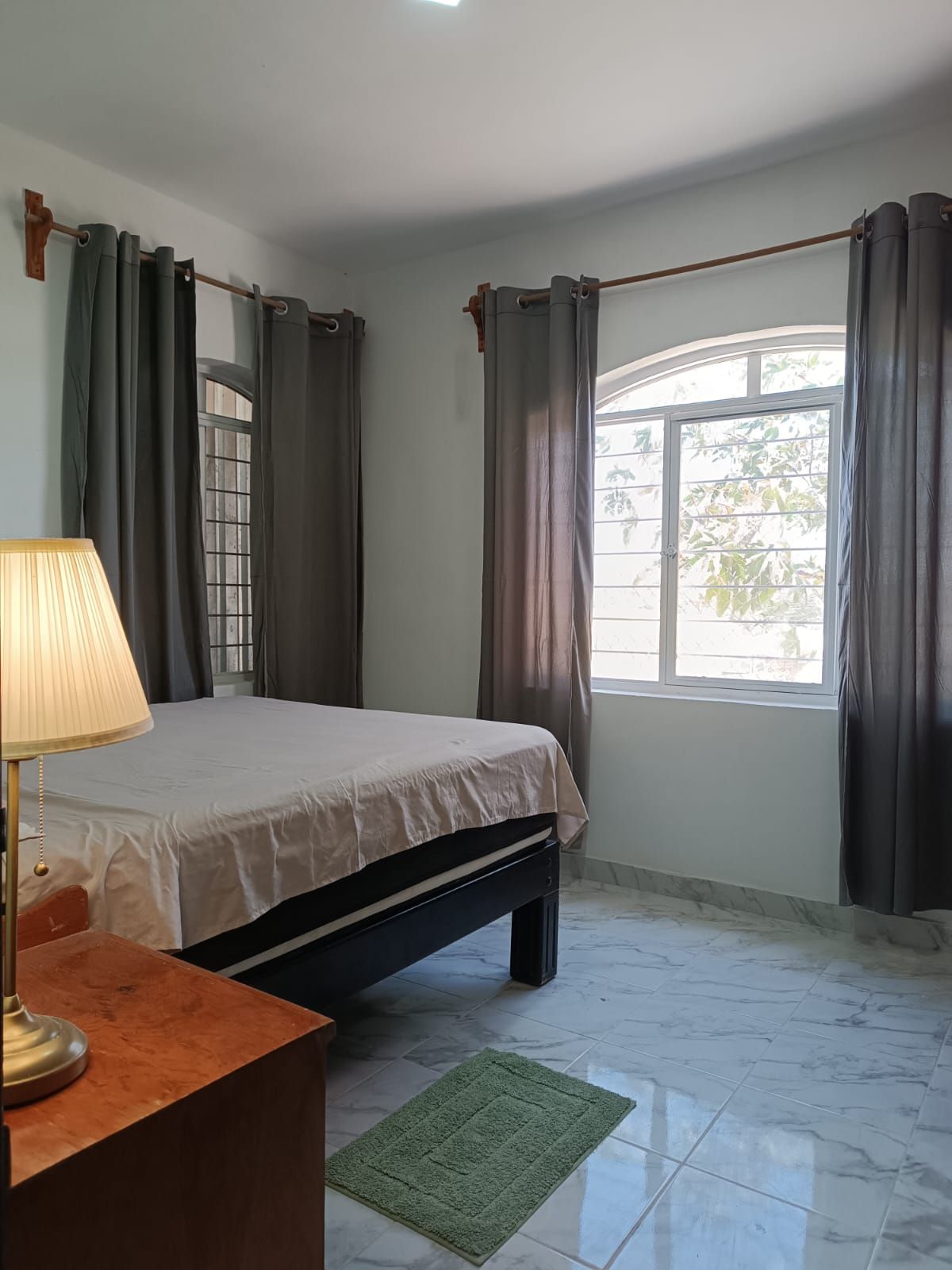 Un dormitorio con cama, escritorio, lámpara y ventana con cortinas.