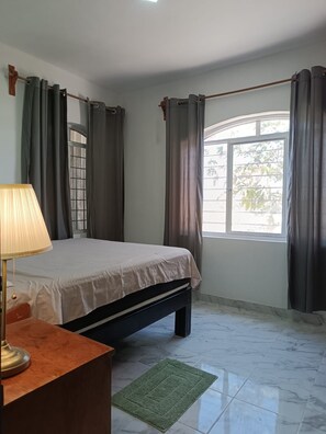 A bedroom with a bed, a desk, a lamp, and a window with curtains.