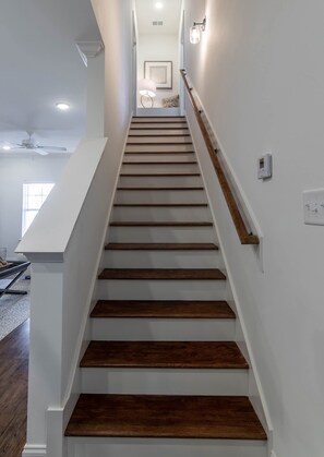 A staircase with wooden steps and white walls, leading to a landing with a ceiling fan and a framed picture. - Cottage Grove Haven (Oxford)