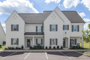 A multi-story residential building with a symmetrical facade, a central entrance with a door and window, and a parking lot in front. - Cottage Grove Haven (Oxford)