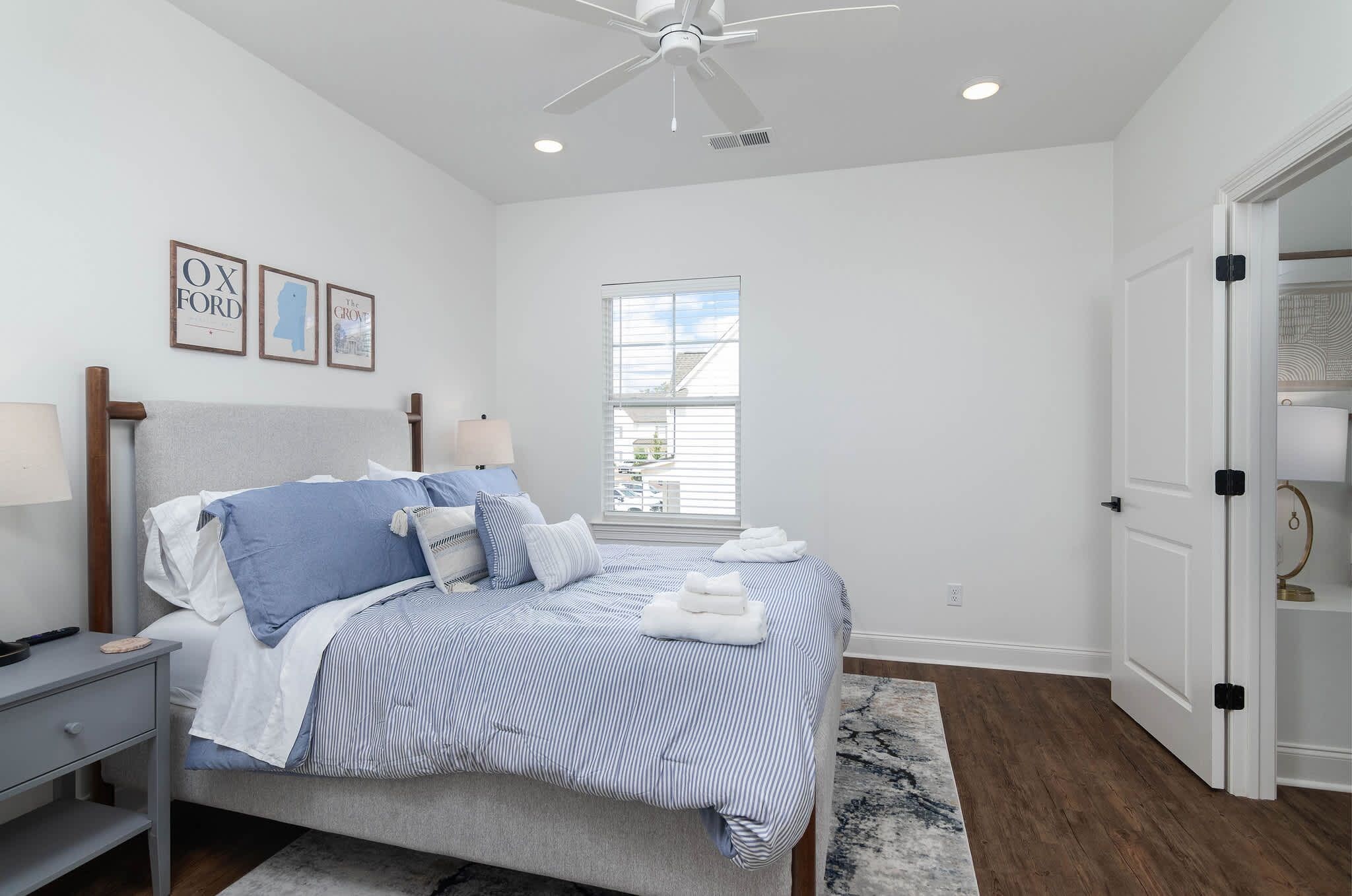 A bedroom with a bed, bedside table, lamp, ceiling fan, window, and a door.