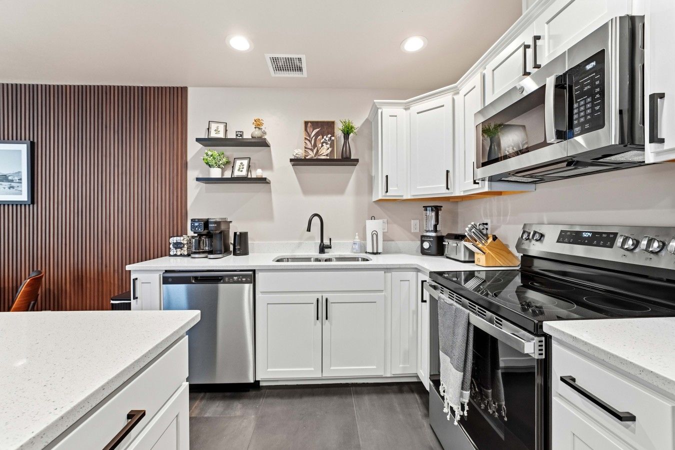 A modern kitchen with white cabinetry, a dishwasher, a stove, and a microwave.