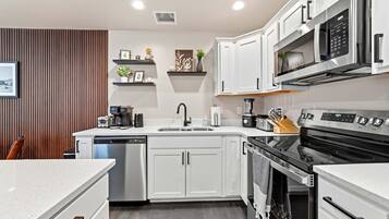 A modern kitchen with white cabinetry, a dishwasher, a stove, and a microwave.