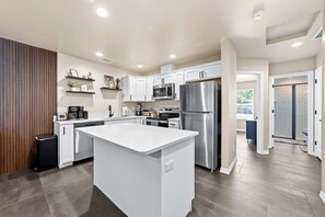 A modern kitchen with white cabinetry, stainless steel appliances, and a central island. - Remote Work Stay with Desk + Private Laundry (Kingman)