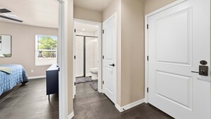 Un couloir donnant sur une chambre avec un lit et un bureau, ainsi qu’une salle de bain équipée de toilettes et d’une douche.