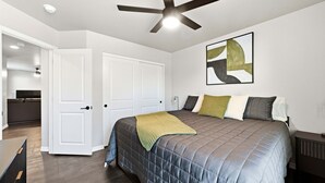 Une chambre à coucher avec un lit, un ventilateur de plafond, une porte et un tableau accroché au mur.