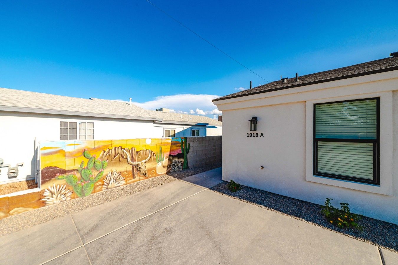 A residential property with a white exterior, a number '1918 A' on the wall, and a mural of desert flora and fauna on the adjacent wall.