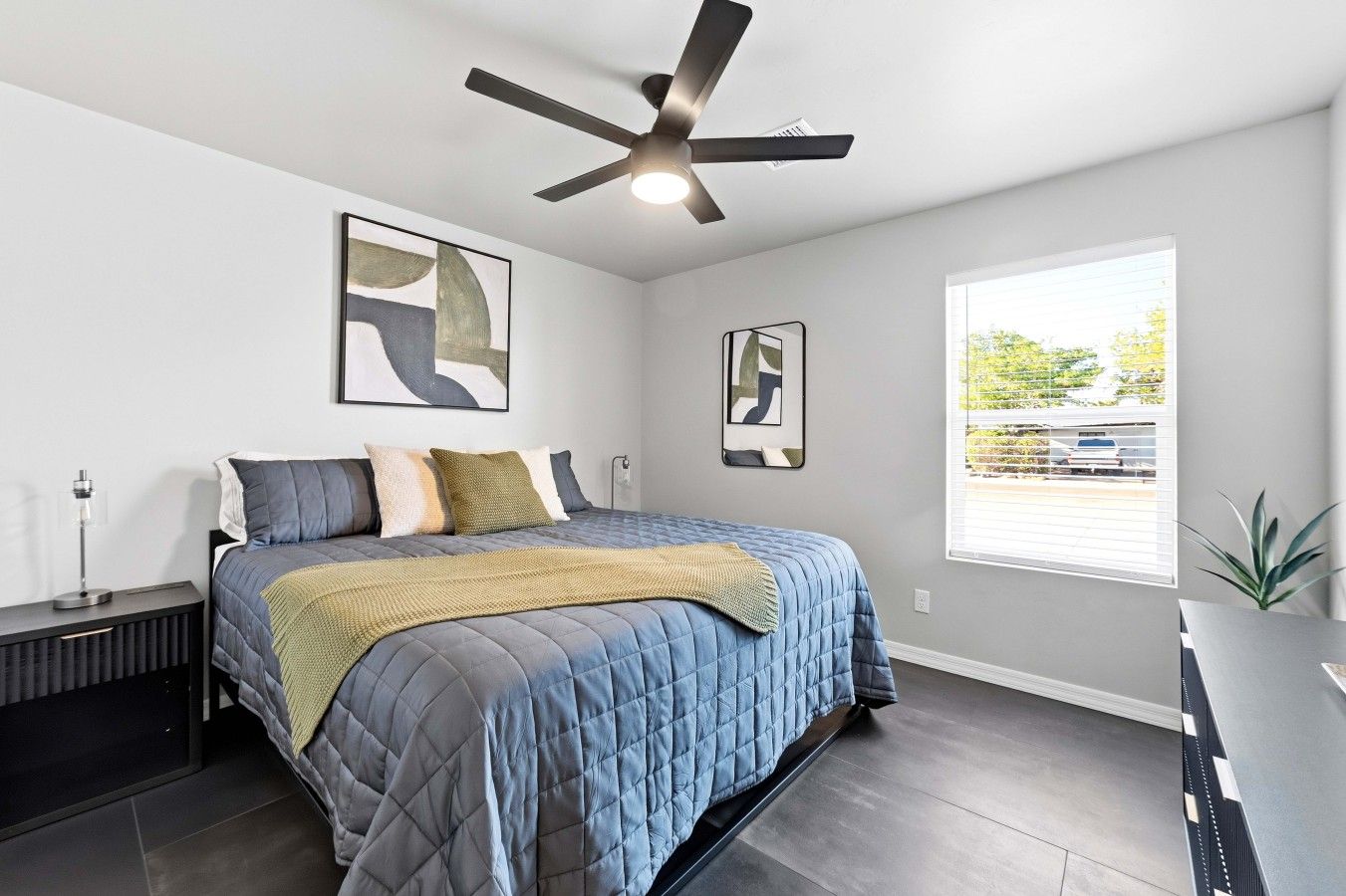 A bedroom with a bed, a ceiling fan, artwork on the walls, and a window with a view.