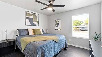 A bedroom with a bed, a ceiling fan, artwork on the walls, and a window with a view.