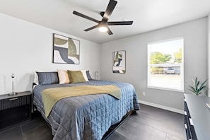 A bedroom with a bed, a ceiling fan, artwork on the walls, and a window with a view.