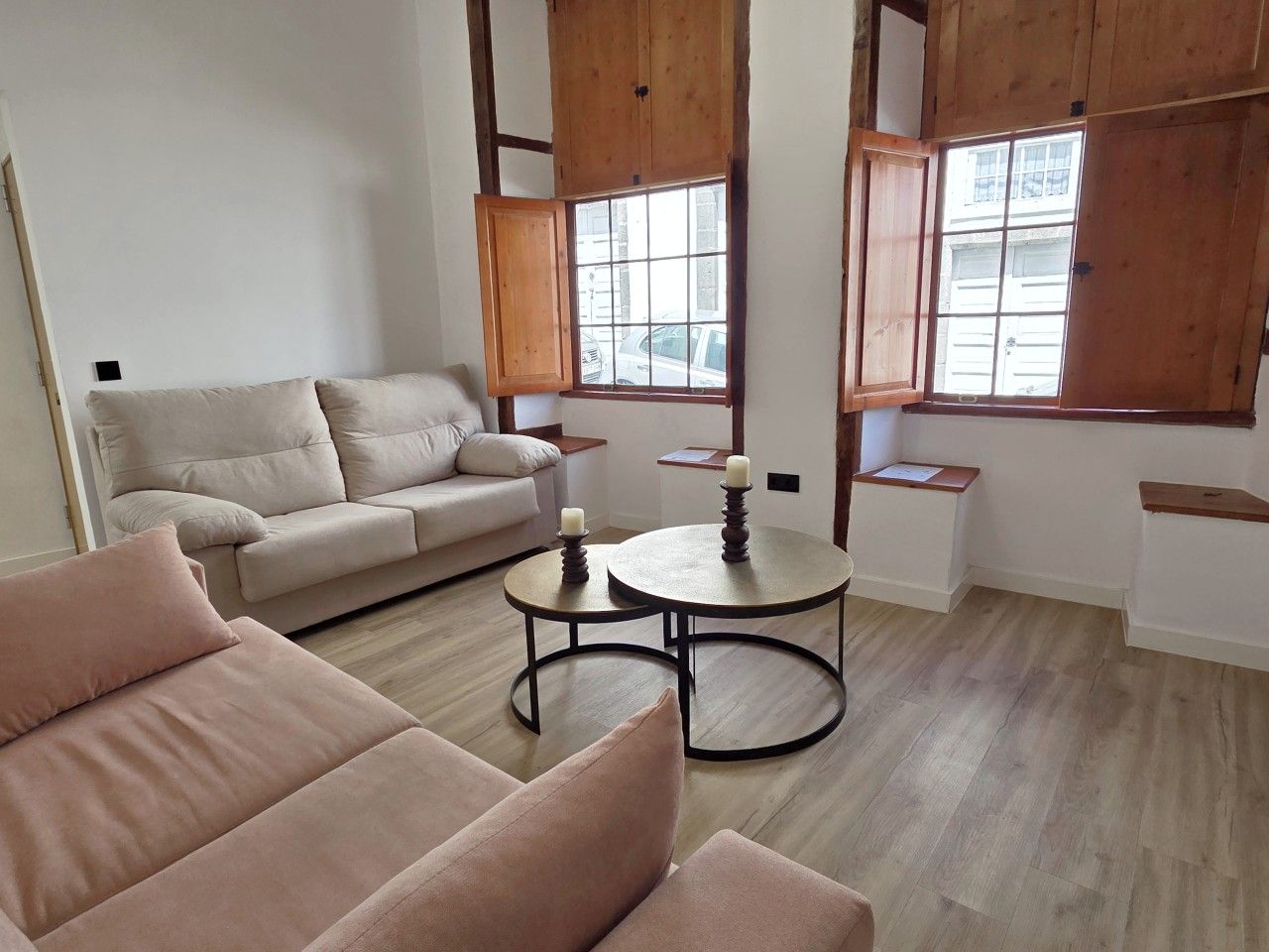 A modern living room with a sofa, a round coffee table, and a window with wooden shutters.