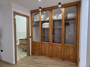 A wooden wardrobe with glass doors, a tiled floor, and a visible bathroom in the background.