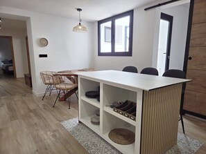 A modern kitchen with a central island, built-in shelves, and a dining area with chairs and a table.