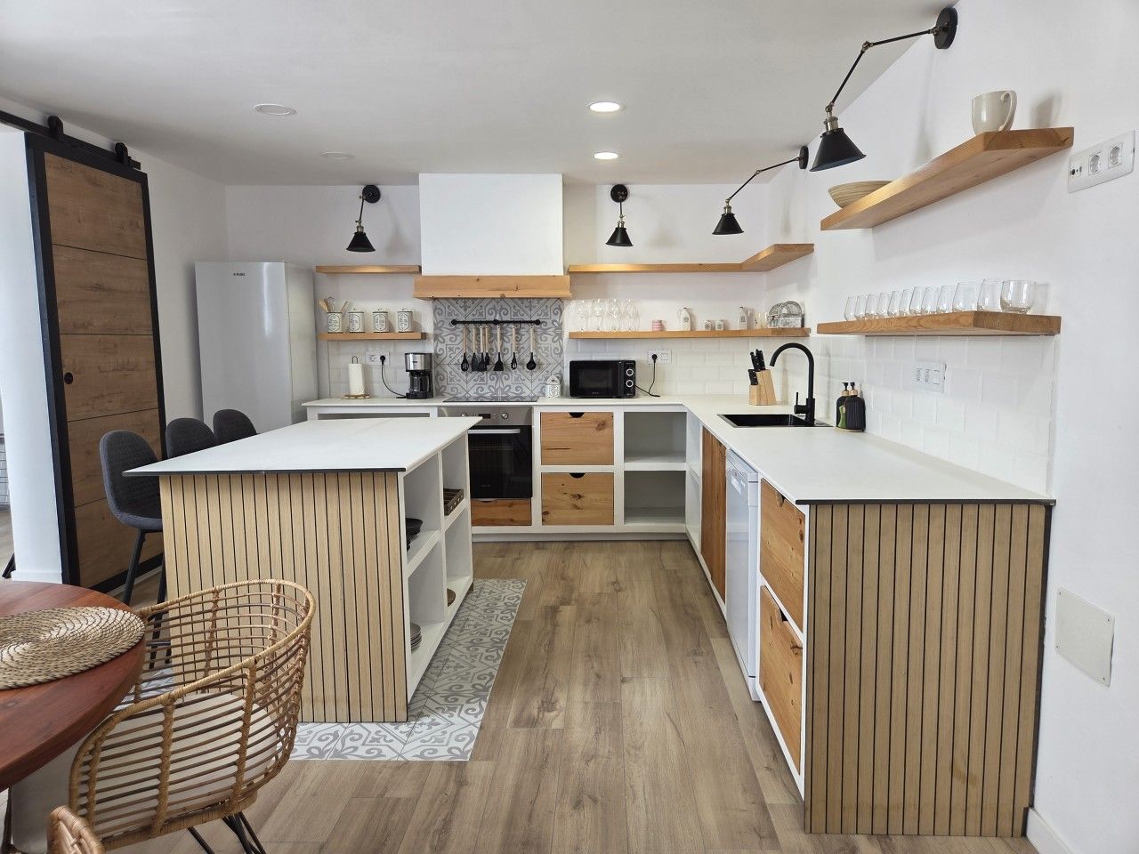 Une cuisine compacte avec des meubles blancs, des éléments décoratifs en bois et un îlot central.