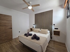 A modern bedroom with a bed, wooden floor, a ceiling fan, and bedside tables.