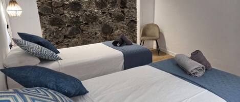 A bedroom with two beds, a stone wall, a chair, and a lamp.