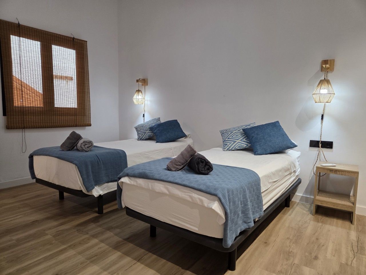 Habitación de hotel con dos camas, suelo de madera e iluminación empotrada.