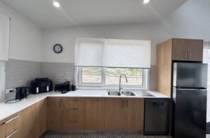 A modern kitchen with wooden cabinets, a stainless steel refrigerator, a dishwasher, and a window with blinds. - Snow and Sun Sanctuary:  East Jindabyne Lakeside escape for Couples or Families. (East Jindabyne)