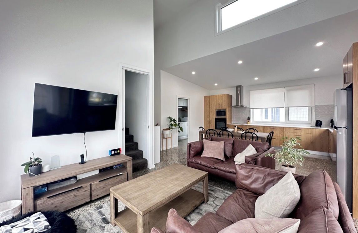 Una sala de estar moderna con un televisor de pantalla plana, una mesa de centro de madera y un sofá de cuero marrón.