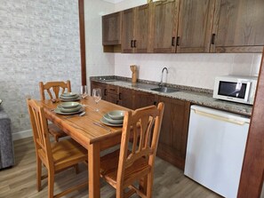 A compact kitchen with wooden cabinets, a granite countertop, a built-in microwave, and a dining table set for four. - Azul, 49 Casa Lago, on the waterfront (Breña Baja)