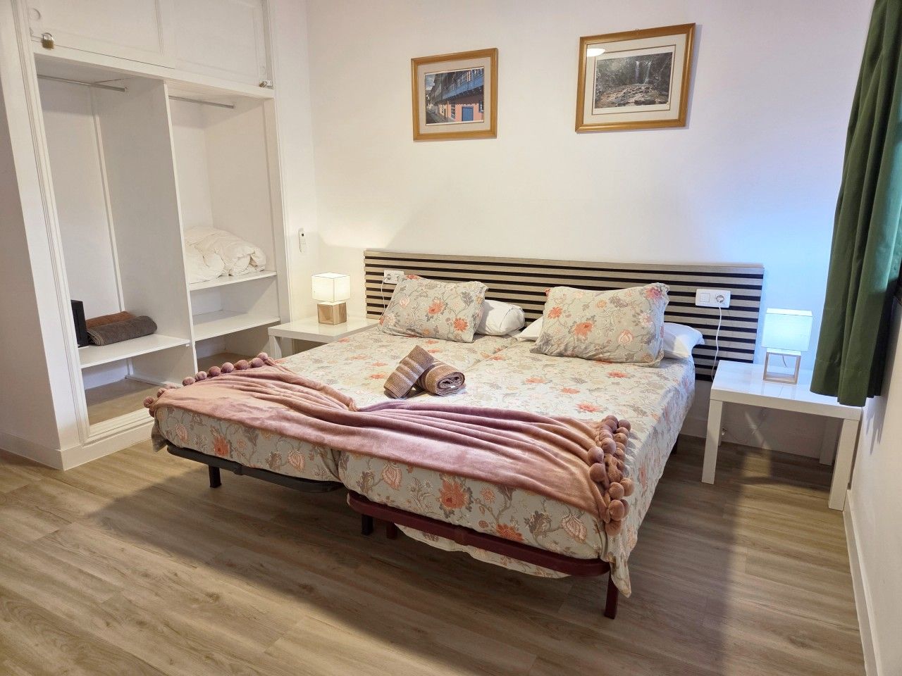 Un dormitorio con una cama, mesitas de noche, un armario y dos cuadros en la pared.