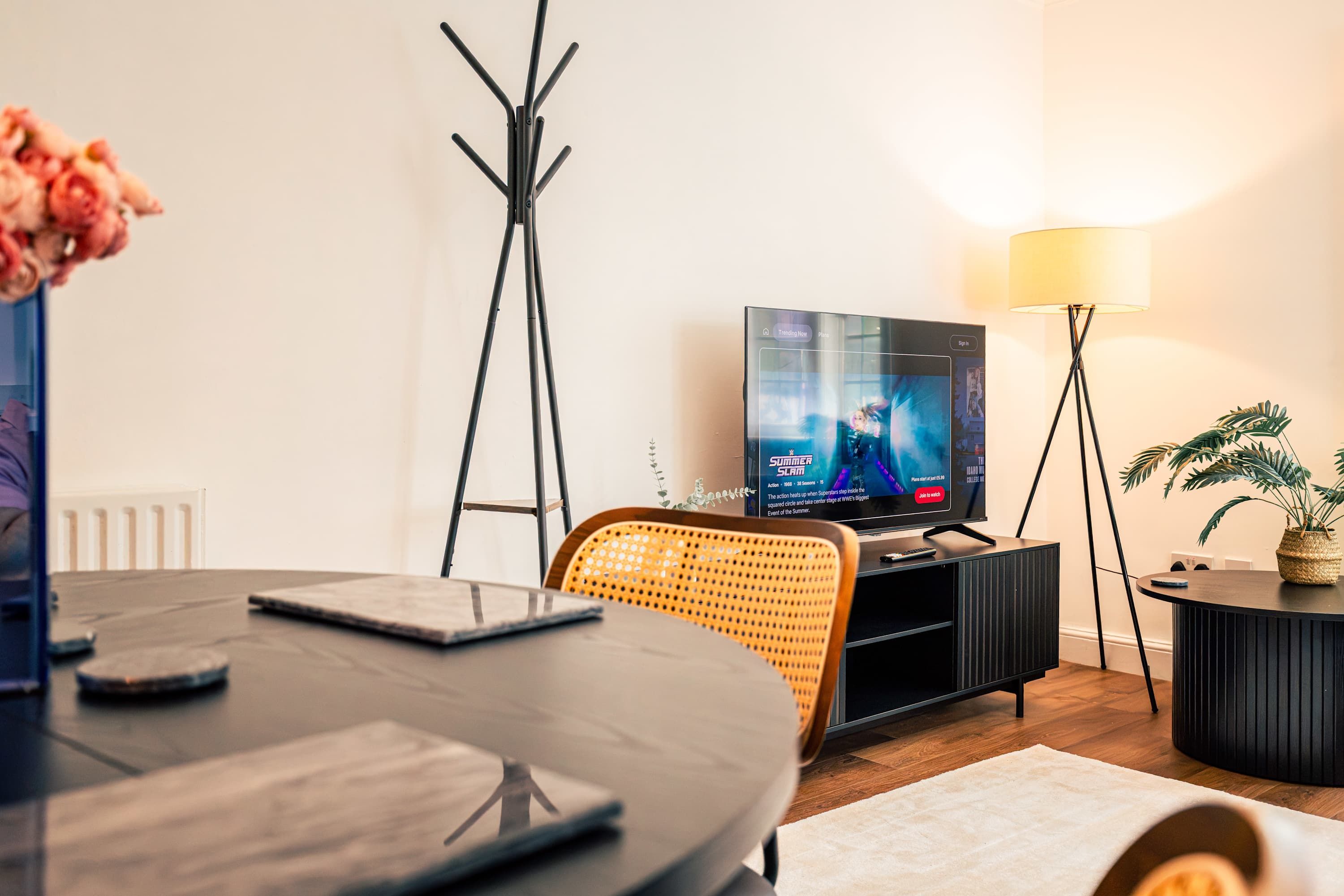 Moderni olohuone, jossa on televisio, ruokapöytä, lattiavalaisin ja ruukkukasvi.