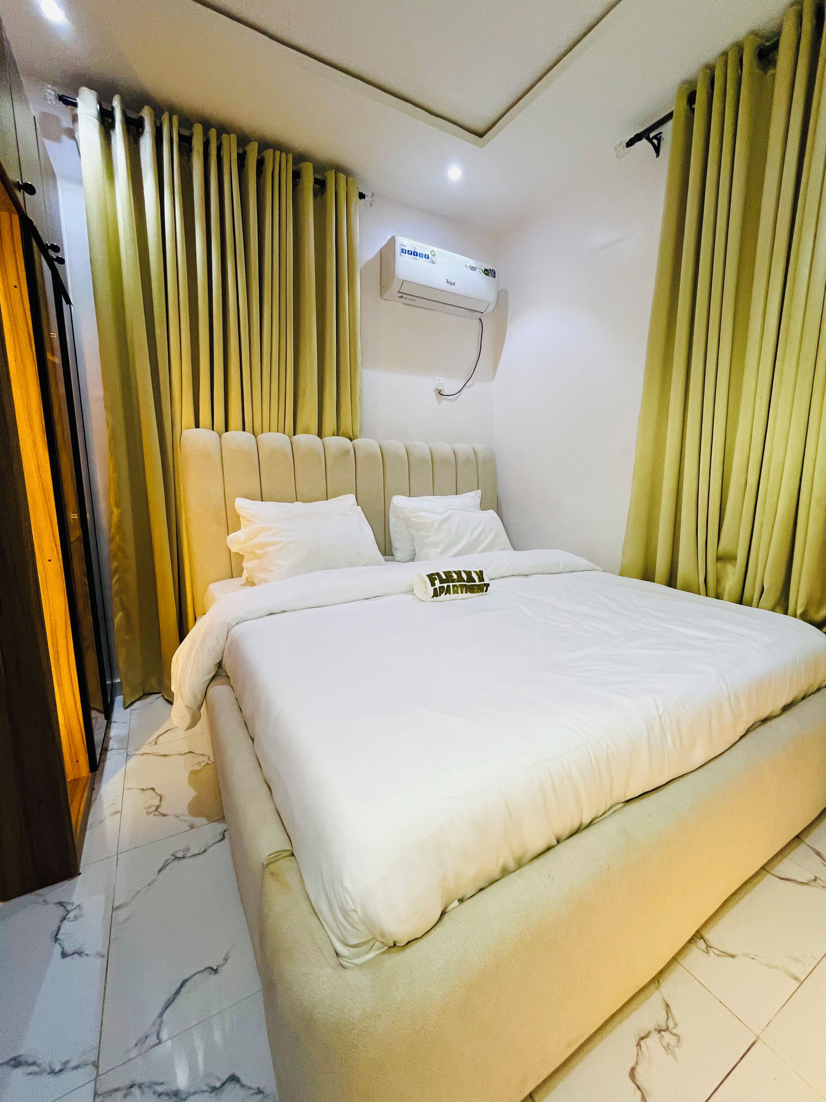 Habitación de hotel con una cama grande, cabecera, aire acondicionado de pared y cortinas.