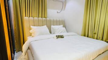 Habitación de hotel con una cama grande, cabecera, aire acondicionado de pared y cortinas.