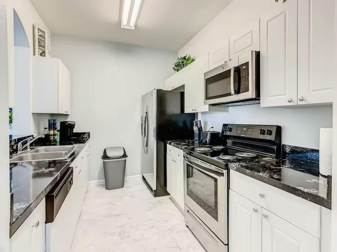 Une cuisine moderne avec des meubles blancs, un réfrigérateur en acier inoxydable, un four à micro-ondes, une cuisinière et un évier.