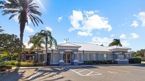 A building with a symmetrical facade, large windows, and a parking lot with marked spaces. - 3BR Resort Condo Windsor Palms Near Disney (Kissimmee)