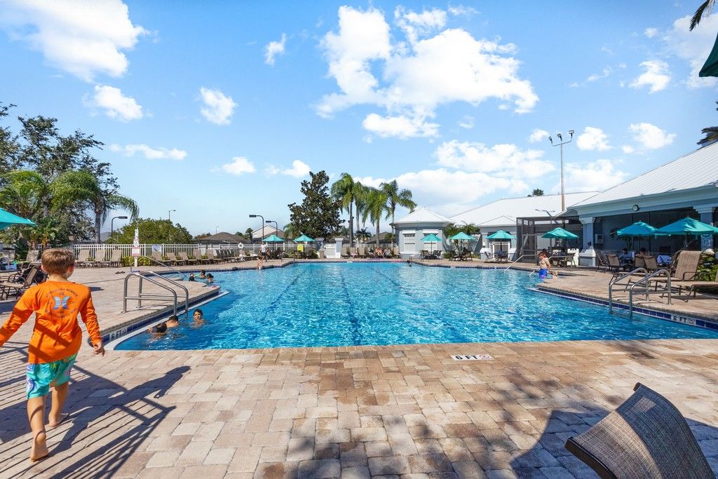 Piscina com deck revestido, espreguiçadeiras e guarda-sóis.