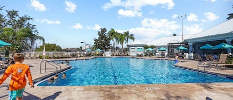 A swimming pool with a tiled deck, lounge chairs, and umbrellas.