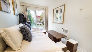 A bedroom with a bed, a bedside table, a radiator, and a window with curtains. - Eastlake Guest Suite near SLU with Private Patio (Seattle)