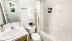 A bathroom with a white sink, toilet, and bathtub. There is a towel rack with a white towel and a basket of toiletries. - Eastlake Guest Suite near SLU with Private Patio (Seattle)
