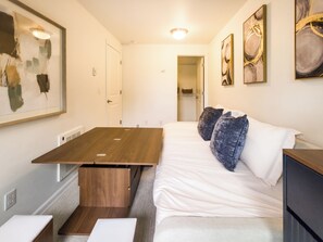 Habitación de hotel con una cama, una mesa de madera, un banco y obras de arte en las paredes.