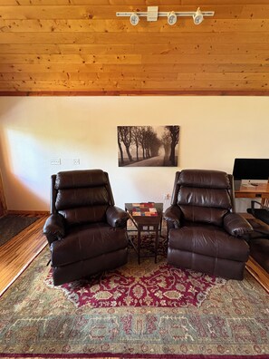 Ein Zimmer mit zwei Ledersesseln, einem kleinen Tisch, einem gemusterten Teppich und einem gerahmten Bild an der Wand.