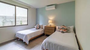Een slaapkamer met twee bedden, een nachtkastje, een lamp en een raam.