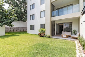 A modern two-story building with a flat roof, a balcony with glass railings, and a small garden area with grass and potted plants. - Vrbo Property (Cuernavaca)