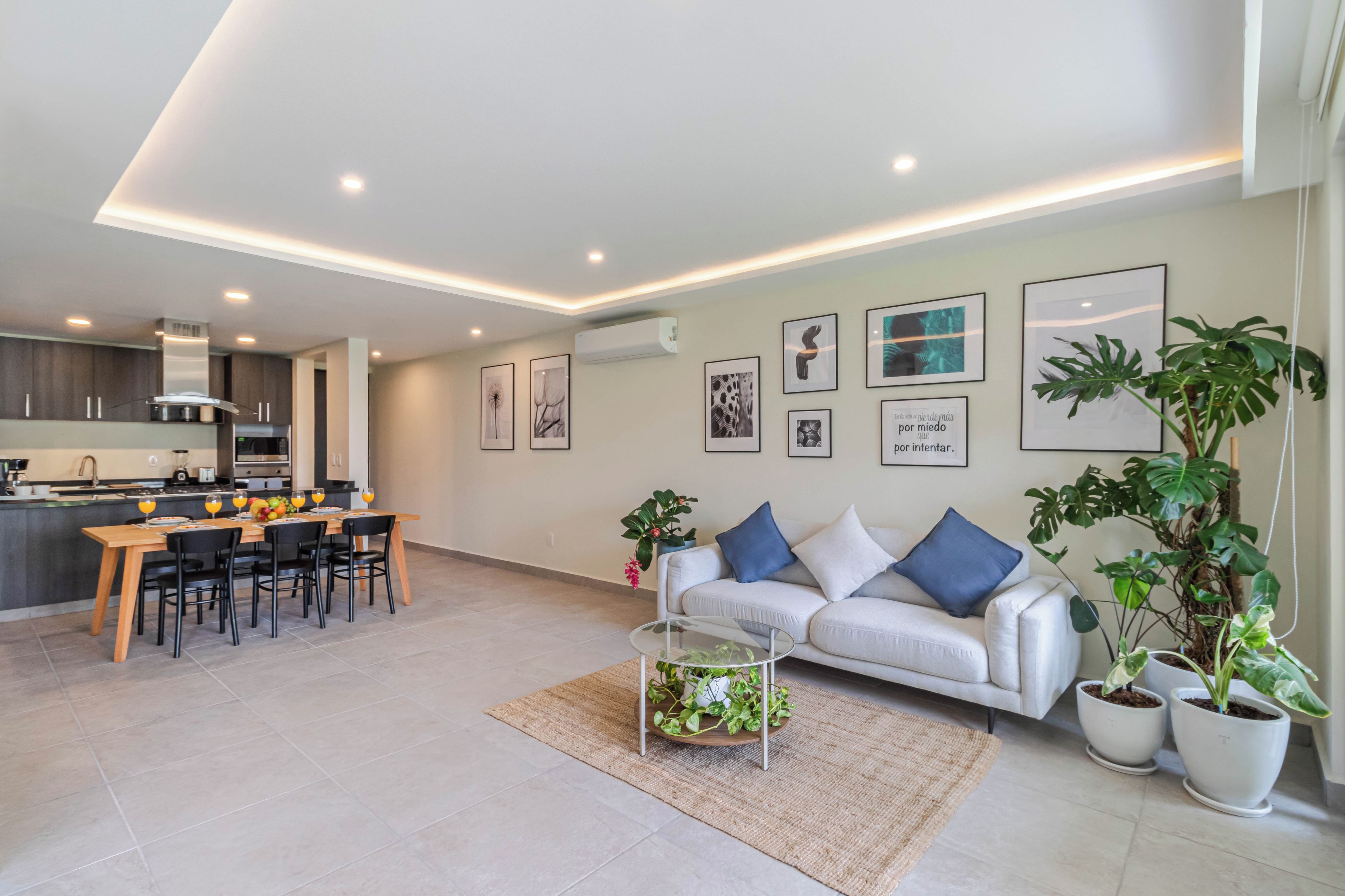 A modern living space with a dining area, kitchen, and a sofa with decorative pillows.