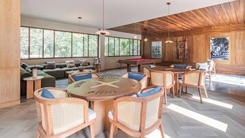 A spacious living area with a pool table, comfortable seating, and large windows offering views of greenery.