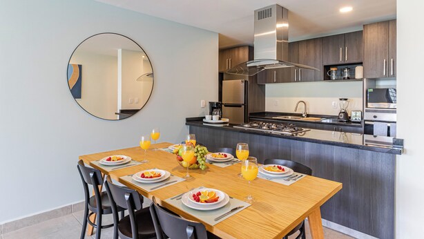 Een moderne keuken met een centraal eiland, roestvrijstalen apparatuur en een eetgedeelte met een houten tafel en stoelen.